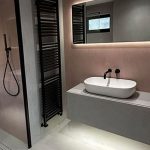 Moderna kopalnica z umivalnikom, ogledalom z osvetlitvijo in črnim radiatorjem za brisače.