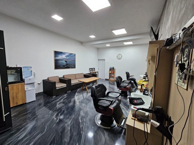 Notranjost frizerskega salona s črnimi stoli, čakalnico in sliko na steni. BRI DECO.